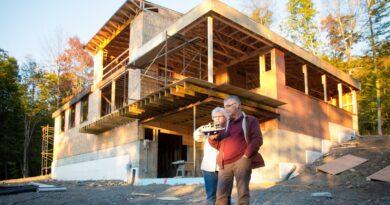 Senior couple stands in front of custom home carcass