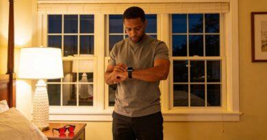 1. A man checking his Apple Watch, with gloojo Night Ease™ Sleep Glasses on the nightstand